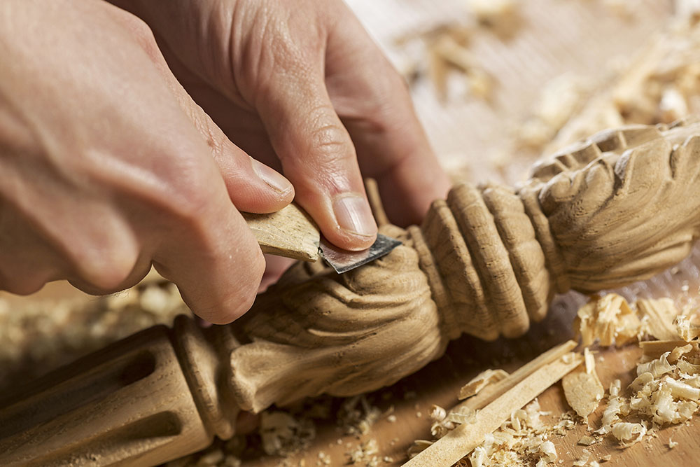 Отблизо ръцете на дърводелец, работещи с нож в ателието му